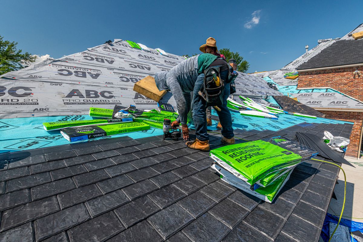 Roofing materials and workers on a partly covered residential roof