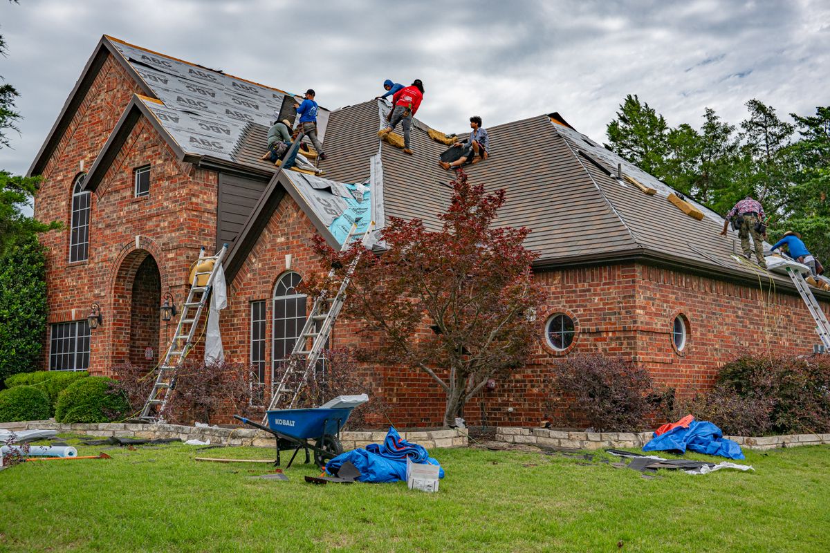 Roofers removing and replacing material on a brick house roof