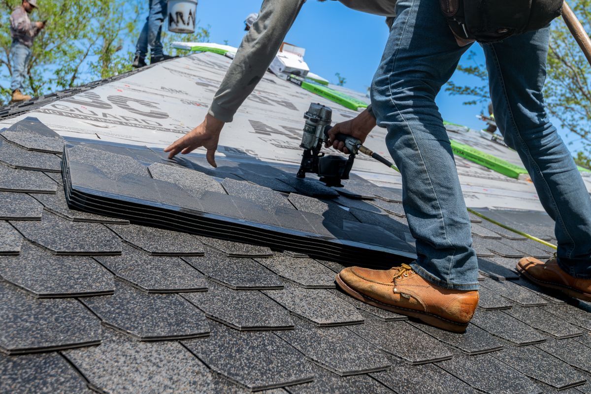 Hands fastening architectural asphalt shingles with a nail gun